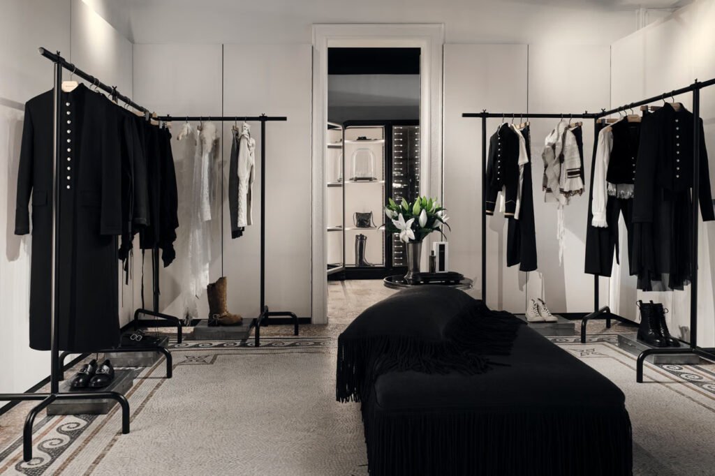Ann-Demeulemeester-Palais-Royal-store-in-Paris-with-a-fringed-black-bench-garment-rails-and-a-doorway-to-a-lit-display-room