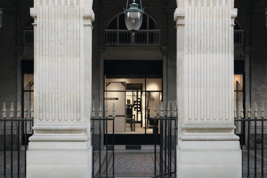 Ann-Demeulemeester-Paris-store-seen-between-fluted-stone-pillars-and-an-iron-gate-at-the-Palais-Royal-under-a-hanging-lantern