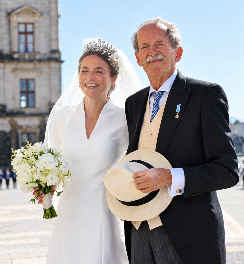 Duchess of Coimbra in diamond tiara and veil holding a white bouquet, beside her father in morning dress and medal